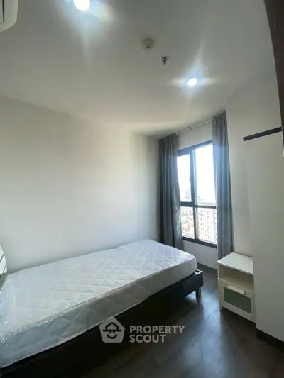 Bright bedroom with large window and modern furnishings in a high-rise apartment.