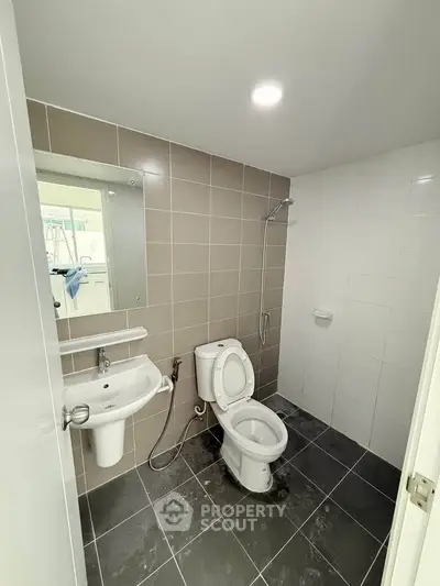 Modern bathroom with sleek fixtures and neutral tiles, featuring a shower and toilet.