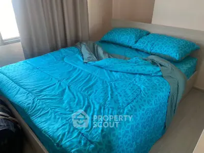 Cozy bedroom with vibrant blue bedding and natural light from window.
