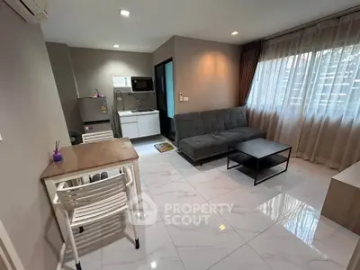 Modern living room with sleek furniture and natural light, featuring a compact kitchen area.