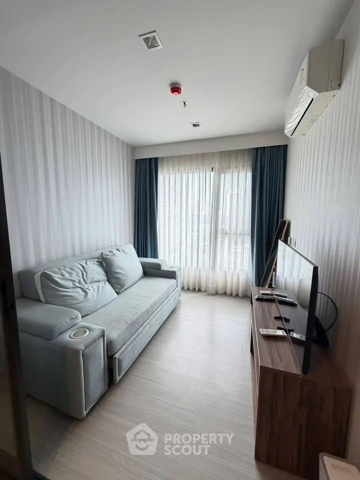 Cozy living room with modern sofa and flat-screen TV, featuring natural light from large window.