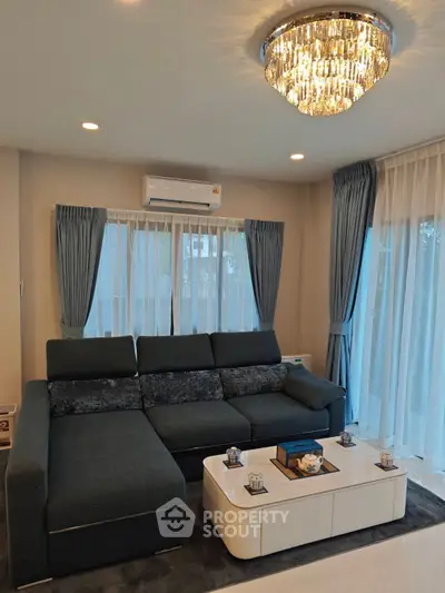 Elegant living room with modern sofa and chandelier, featuring large windows and stylish curtains.