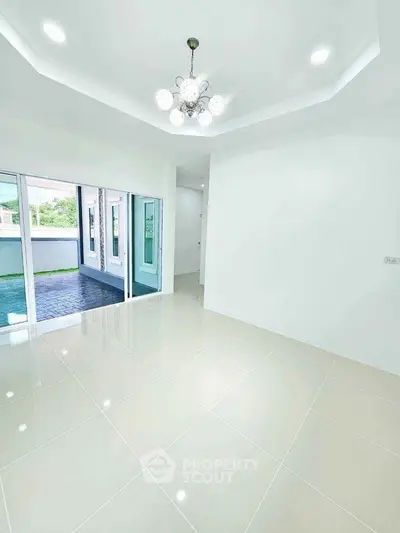 Spacious modern living room with elegant chandelier and large windows opening to a patio.