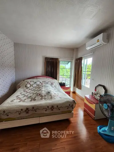 Cozy bedroom with wooden flooring, air conditioning, and a scenic window view.