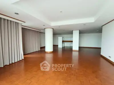 Spacious open-plan living area with wooden flooring and large windows.