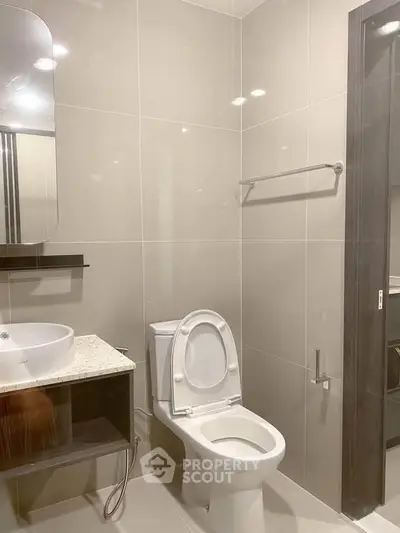 Modern bathroom with sleek fixtures and neutral tiles, featuring a stylish vanity and toilet.