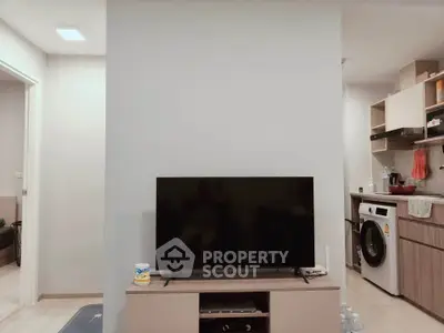 Modern living room with TV and adjacent kitchen featuring washing machine and open shelving.