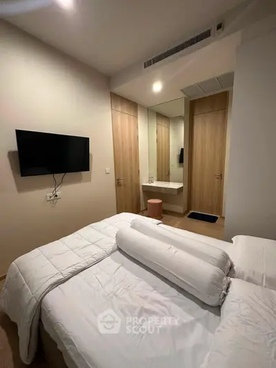 Modern bedroom with sleek design, featuring a wall-mounted TV and cozy bedding, perfect for relaxation.