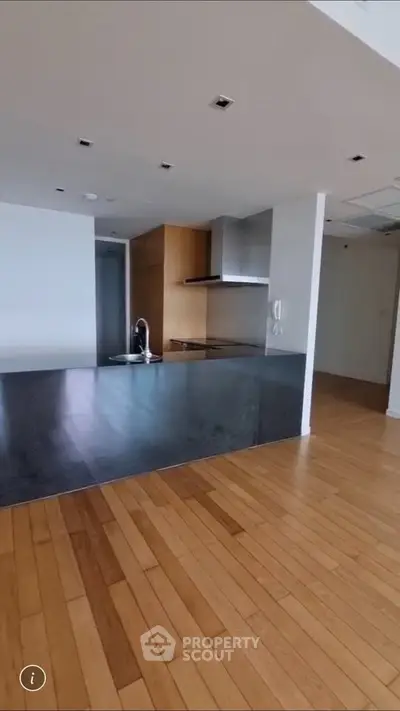 Modern kitchen with sleek black countertop and wooden flooring in open layout apartment.