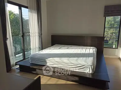 Spacious bedroom with large windows and balcony access, featuring modern wooden bed frame.