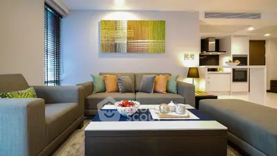 Modern living room with stylish decor and open kitchen layout, featuring cozy seating and contemporary artwork.