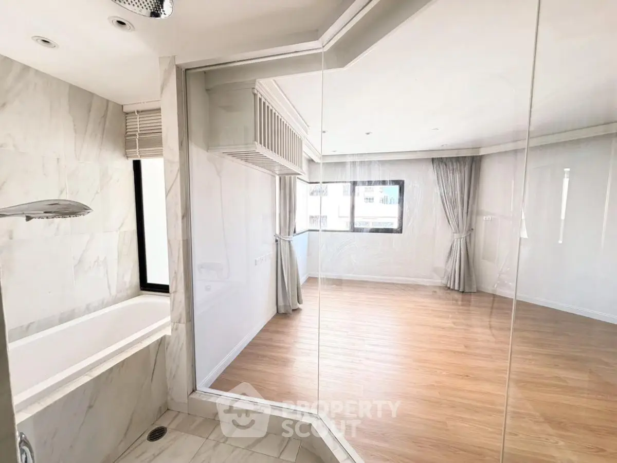 Spacious modern bathroom with glass partition and wooden flooring