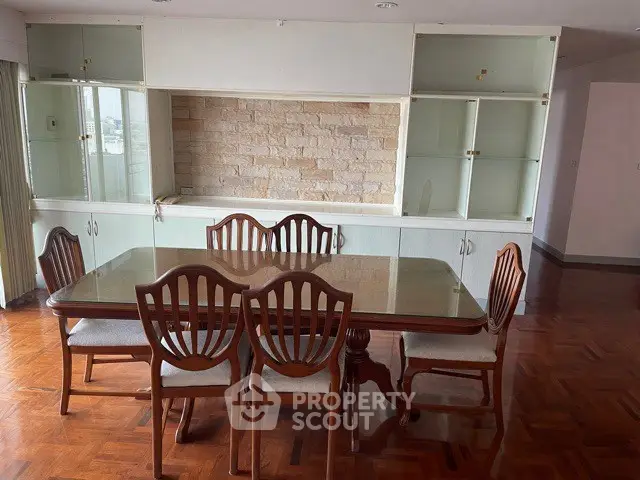 Spacious dining area with elegant wooden table and chairs, featuring built-in glass cabinets and parquet flooring.