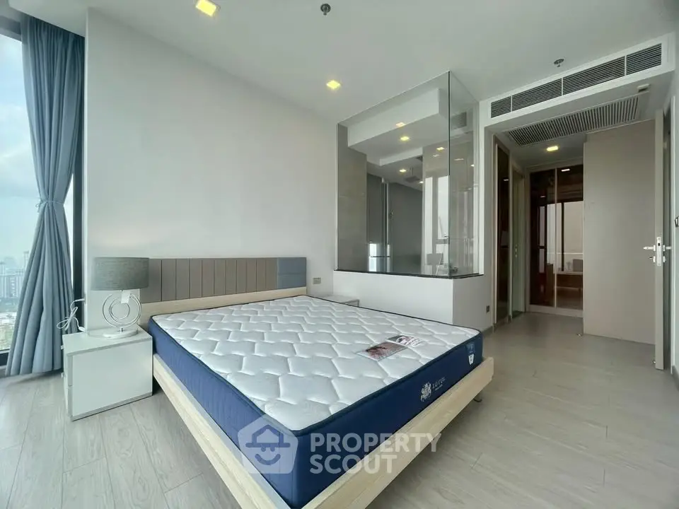 Modern bedroom with large window and city view, featuring a stylish bed and sleek design.