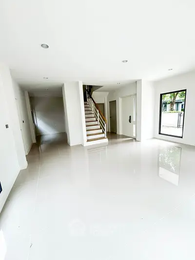 Spacious modern living room with glossy white tiles and staircase, large windows for natural light.