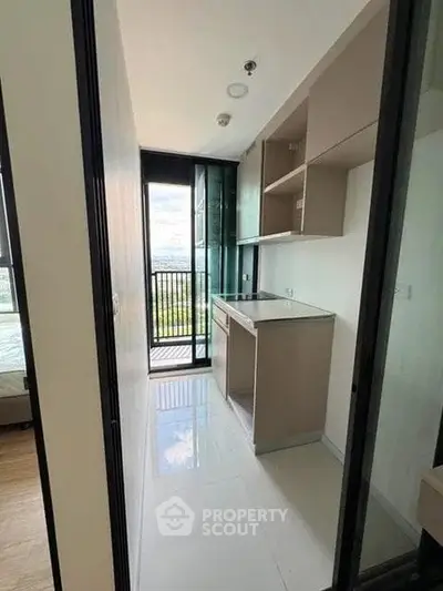 Modern compact kitchen with sleek cabinetry and balcony view in urban apartment.