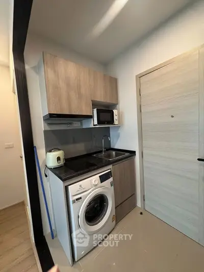 Compact modern kitchen with washing machine and microwave in sleek apartment.
