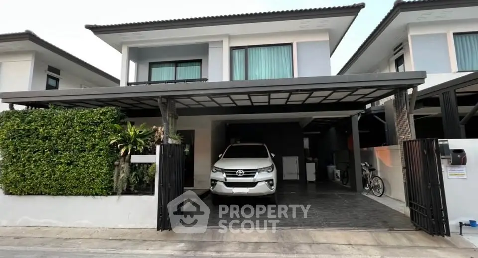 Modern two-story house with carport and lush greenery in a suburban setting.