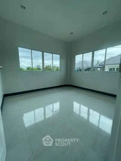 Spacious empty room with large windows and glossy tiled floor, offering ample natural light and serene views.