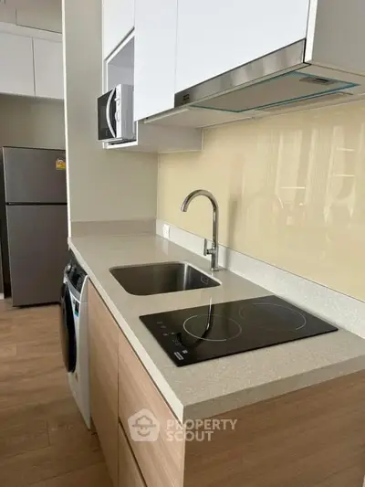 Modern kitchen with sleek countertop, induction stove, and stainless steel appliances.