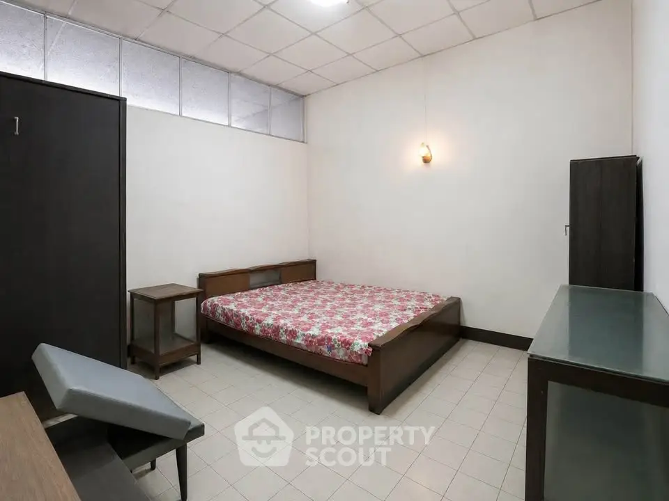Spacious bedroom with minimalist furniture and floral bedspread, perfect for a cozy retreat.