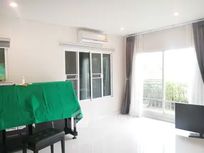 Bright living room with large windows and balcony access, featuring modern air conditioning and elegant curtains.