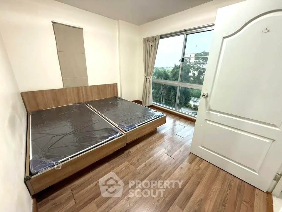 Spacious bedroom with large window and wooden flooring in modern apartment
