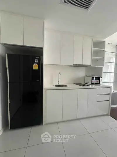 Modern minimalist kitchen with sleek white cabinetry and black fridge in a stylish apartment.