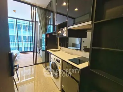 Modern kitchen with sleek black cabinets, washing machine, and open layout leading to a bright living area.