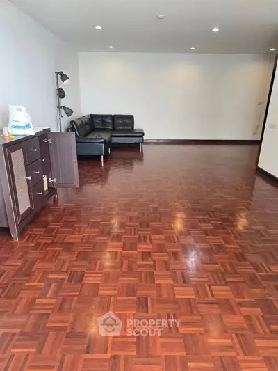 Spacious living room with elegant wooden flooring and modern black leather sofa.