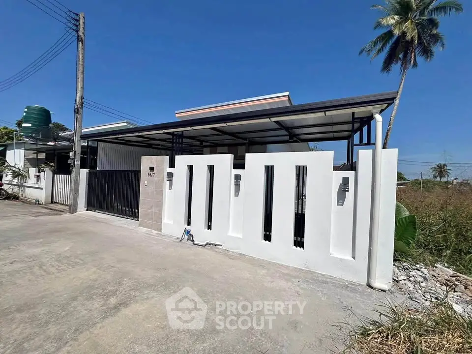 Modern single-story house with sleek white exterior and gated entrance under clear blue sky.