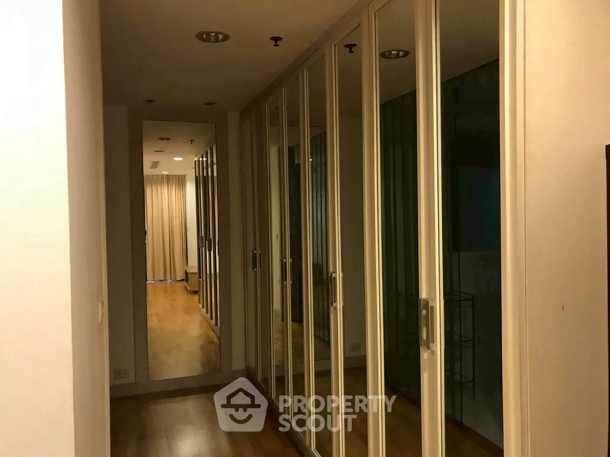 Spacious hallway with mirrored closets and wooden flooring in modern apartment.