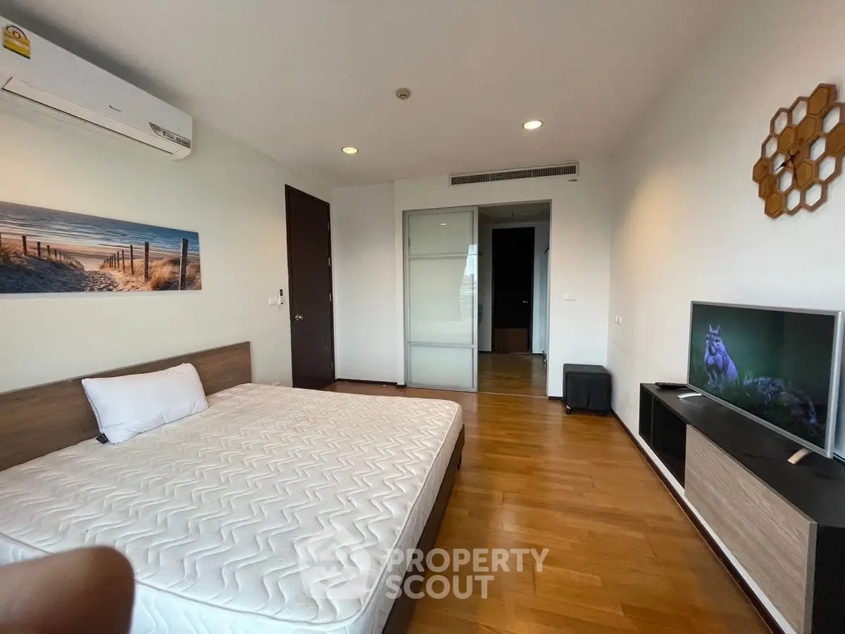 Spacious bedroom with modern decor and wooden flooring, featuring a comfortable bed and wall-mounted TV.