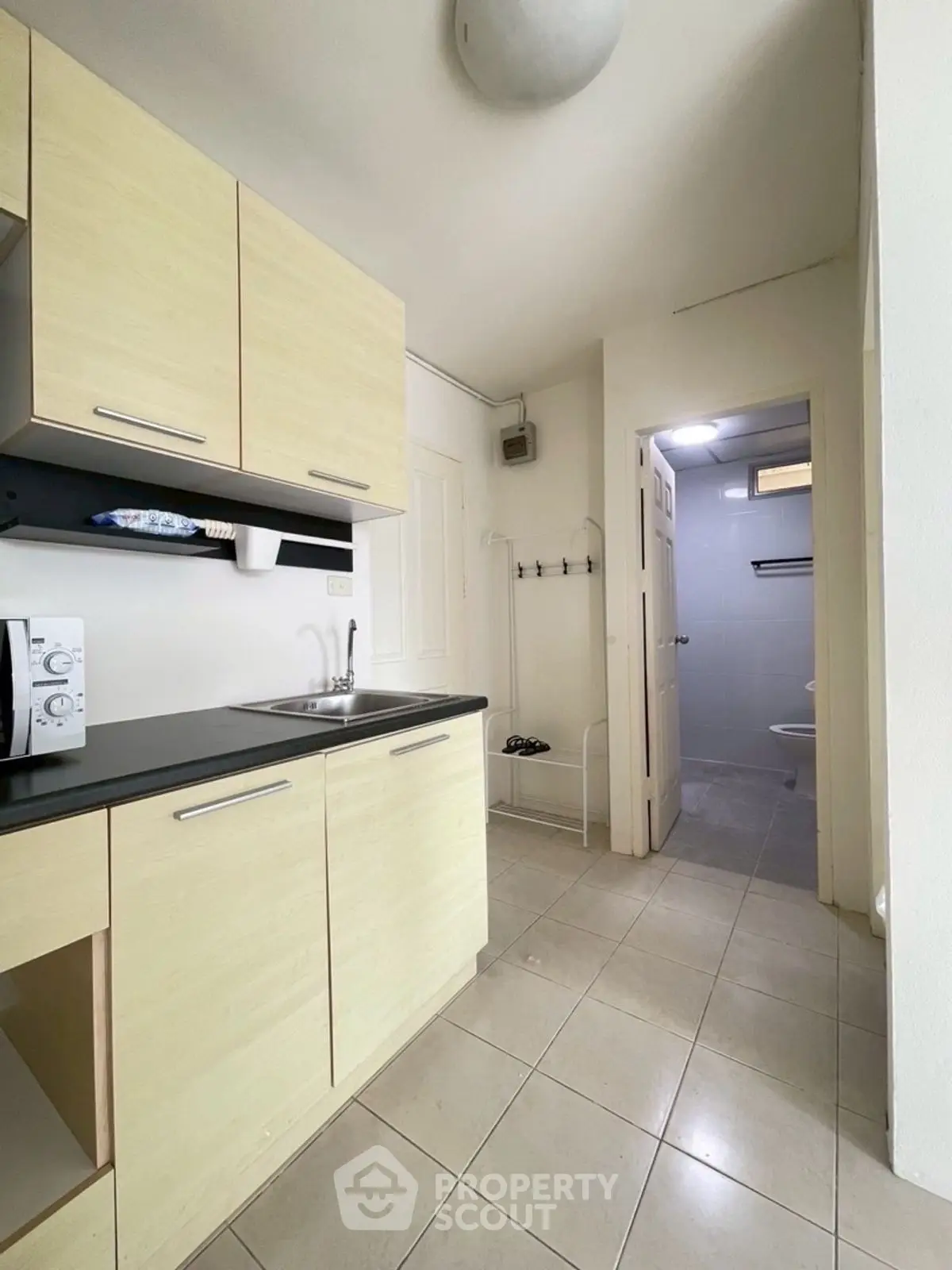 Compact kitchen with light wood cabinets and adjacent bathroom entry