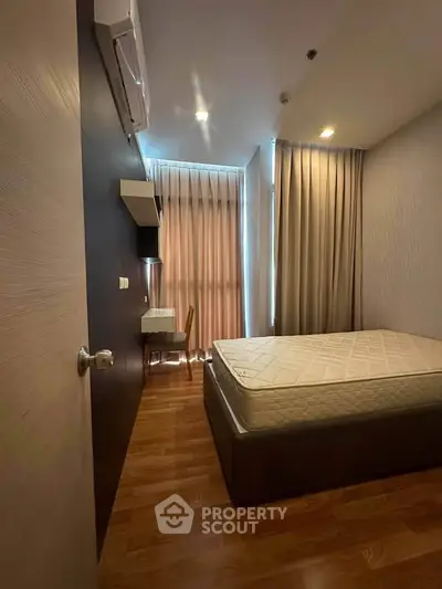 Cozy bedroom with wooden flooring, large window, and modern furnishings.