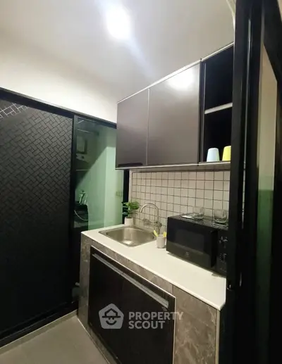 Modern kitchen with sleek cabinetry and compact design, featuring a microwave and stylish backsplash.