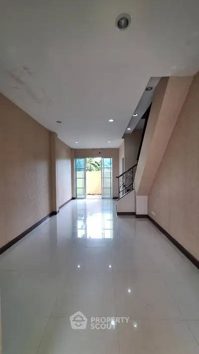 Spacious empty room with glossy tiled floor and staircase, ideal for customization.