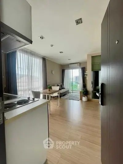 Modern open-plan living room with kitchen, featuring large windows and stylish decor.