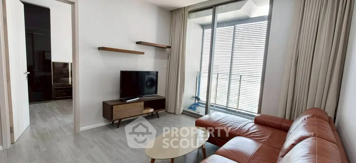 Modern living room with leather sofa and TV, featuring a small balcony with sliding glass doors.