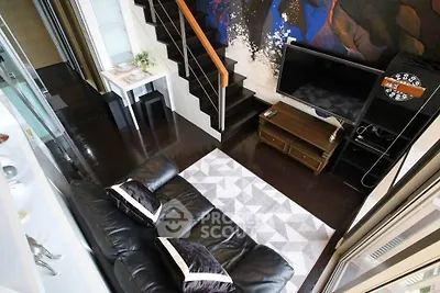 Modern living room with stylish decor and staircase, featuring a cozy black leather sofa and wall-mounted TV.