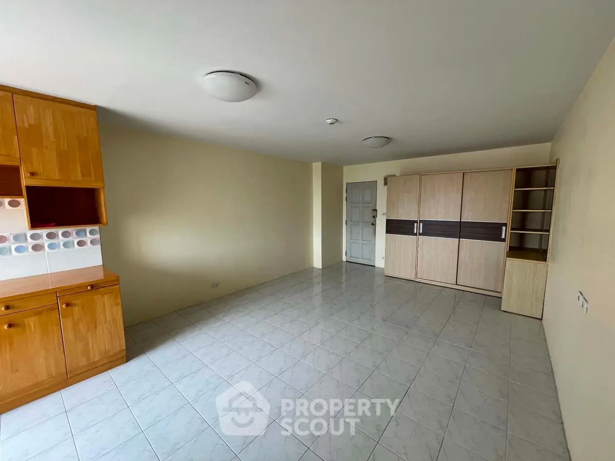 Spacious unfurnished living room with built-in wooden cabinets and tiled flooring.
