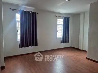 Spacious empty room with wooden flooring and large windows, perfect for customization.