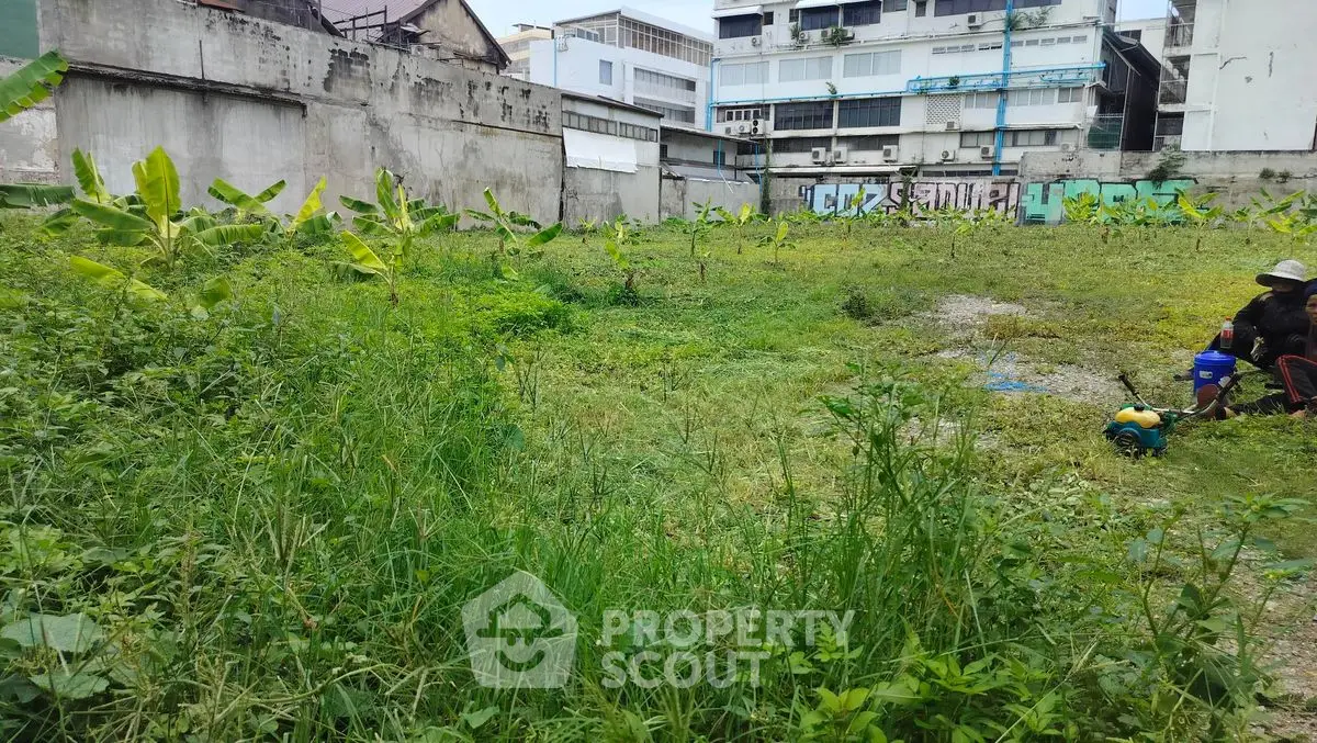 Vacant urban lot with overgrown grass and surrounding buildings, potential for development.