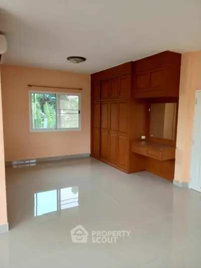 Spacious bedroom with built-in wooden wardrobe and large window view.