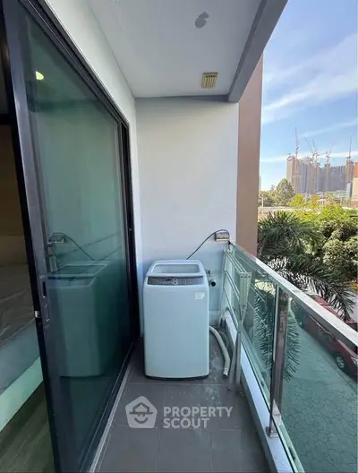 Compact balcony with washing machine and glass railing, offering urban views.