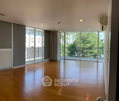 Spacious living room with large windows and wooden flooring, offering a bright and airy atmosphere.