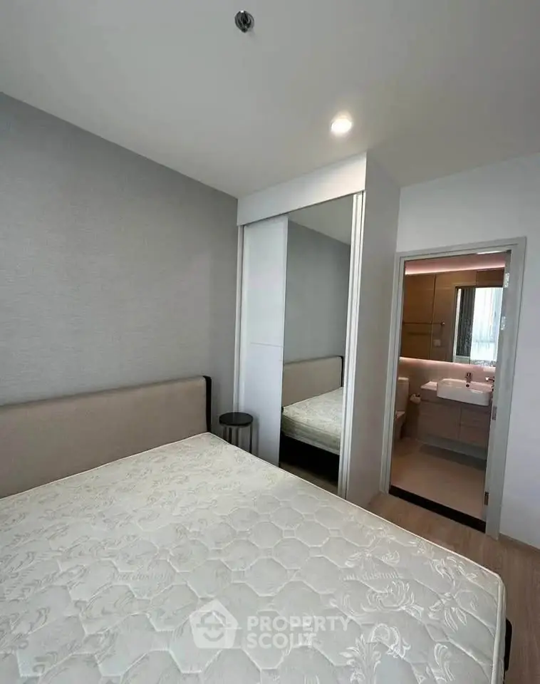 Modern bedroom with mirrored closet and ensuite bathroom in stylish apartment.