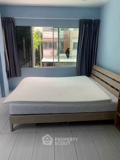 Spacious bedroom with large window and modern bed frame, offering natural light and urban view.