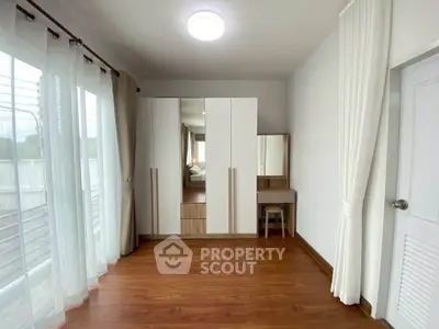 Spacious bedroom with wooden flooring and large wardrobe, featuring natural light from wide windows.