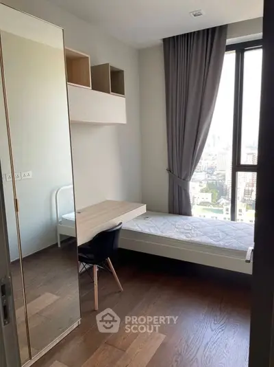 Modern bedroom with city view, featuring a single bed, desk, and large window.